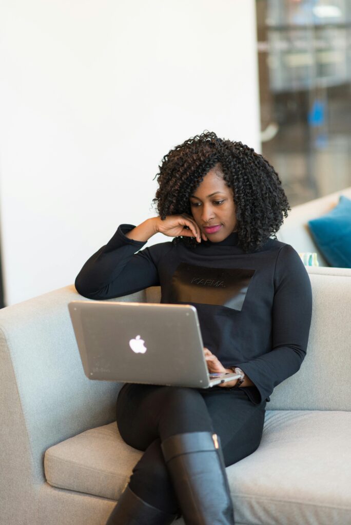 A woman using a laptop while sitting on a sofa in a modern office space.