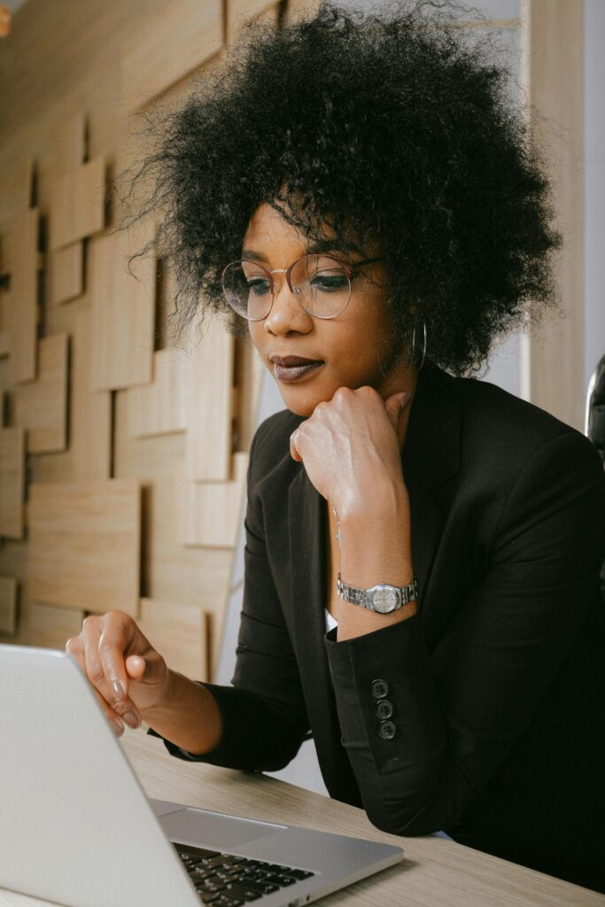 Professional woman with afro hairstyle working on a laptop in a modern office setting.